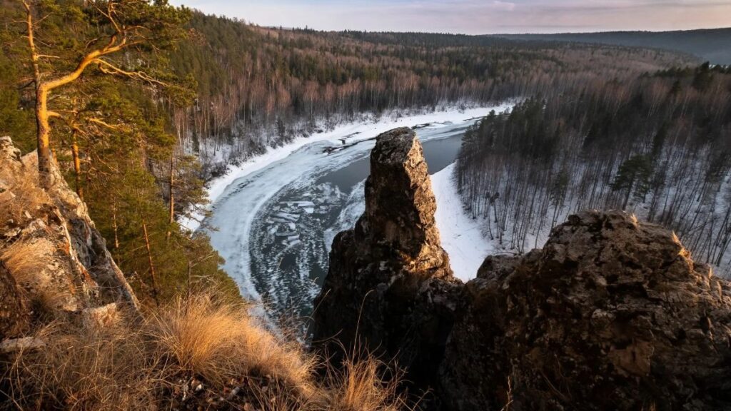 Чусовая ранней весной: излучина реки во льду, скалы и сосны над водой